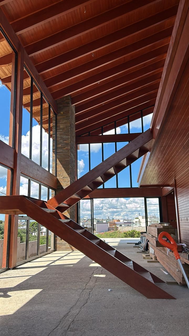 Interior de residência em madeira laminada colada com escada de madeira e grandes janelas